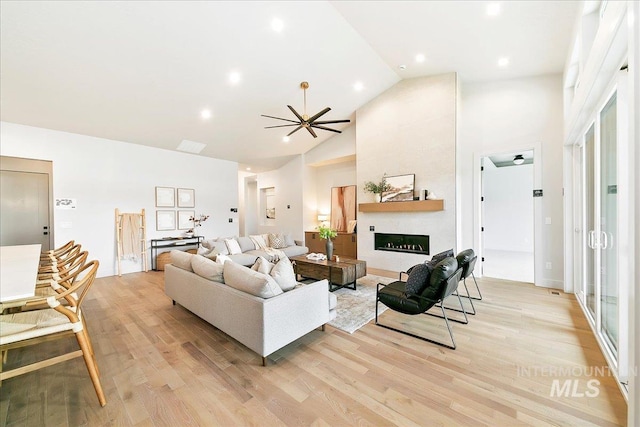 living room with a large fireplace, light hardwood / wood-style floors, high vaulted ceiling, and ceiling fan