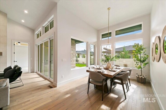 dining area with high vaulted ceiling, light hardwood / wood-style floors, and a notable chandelier