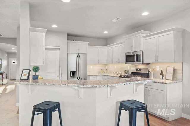 kitchen featuring a kitchen bar, white cabinetry, light stone counters, and appliances with stainless steel finishes