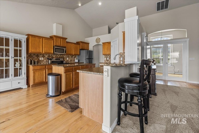 160 Summit Ridge Rd, Horseshoe Bend, ID 83629 - kitchen with stainless steel appliances, brown cabinets, light wood-style floors, high vaulted ceiling, and dark stone countertops
