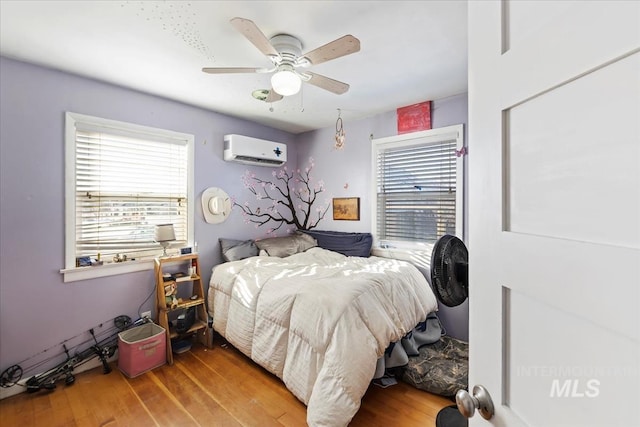 bedroom with multiple windows, wood-type flooring, an AC wall unit, and ceiling fan