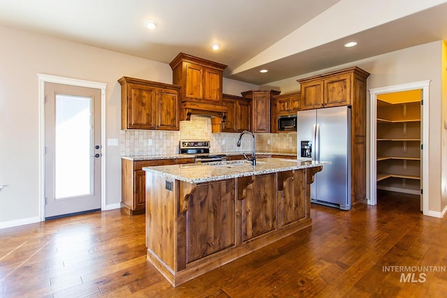 kitchen with light stone countertops, sink, lofted ceiling, a kitchen island with sink, and appliances with stainless steel finishes