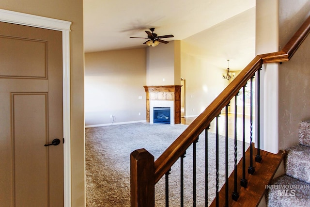 staircase with carpet, ceiling fan with notable chandelier, a fireplace, and vaulted ceiling