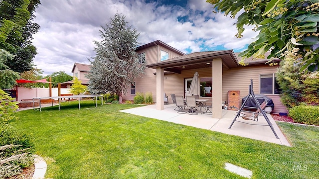 rear view of property featuring a lawn, a trampoline, and a patio