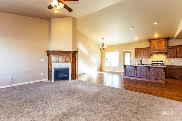 unfurnished living room featuring ceiling fan with notable chandelier, sink, vaulted ceiling, carpet floors, and a tiled fireplace