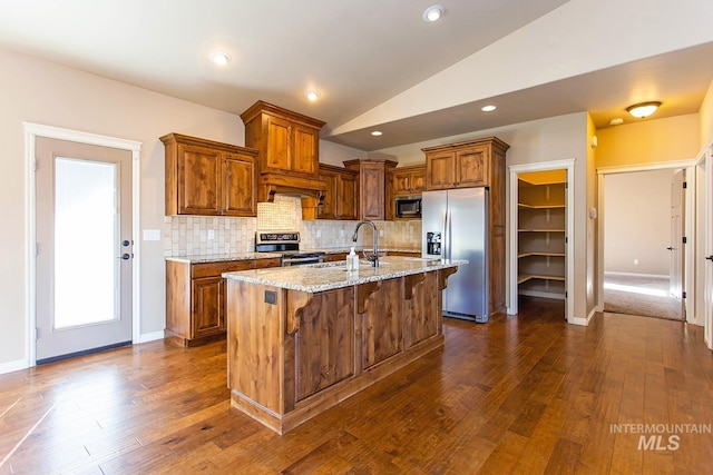 kitchen featuring light stone countertops, appliances with stainless steel finishes, a kitchen island with sink, sink, and lofted ceiling