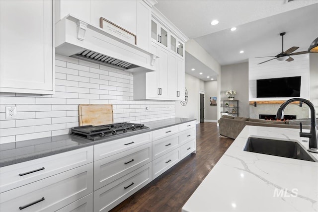 kitchen featuring custom range hood, glass insert cabinets, open floor plan, stainless steel gas cooktop, and a sink