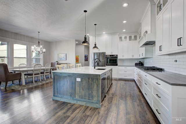 kitchen with a center island with sink, white cabinets, glass insert cabinets, hanging light fixtures, and stainless steel appliances