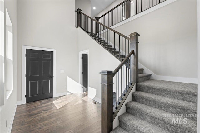 stairway with recessed lighting, visible vents, a towering ceiling, wood finished floors, and baseboards