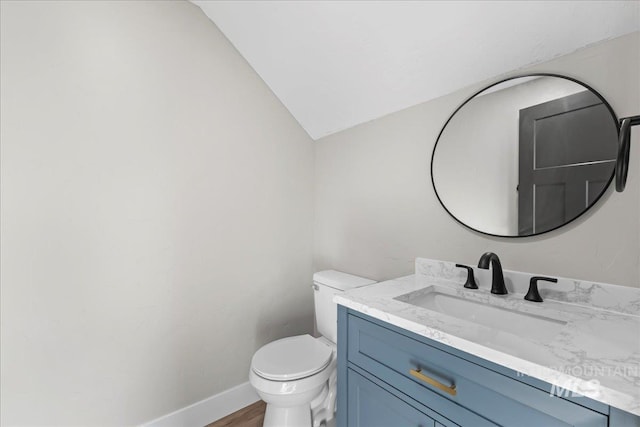 half bath featuring lofted ceiling, toilet, wood finished floors, vanity, and baseboards