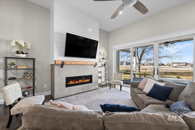 living room with a ceiling fan, a large fireplace, baseboards, and wood finished floors