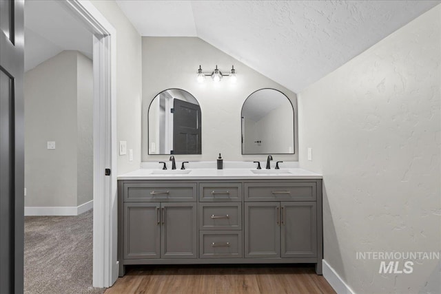 bathroom featuring lofted ceiling, a sink, baseboards, and double vanity