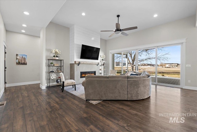 living area with ceiling fan, recessed lighting, a large fireplace, dark wood-type flooring, and baseboards