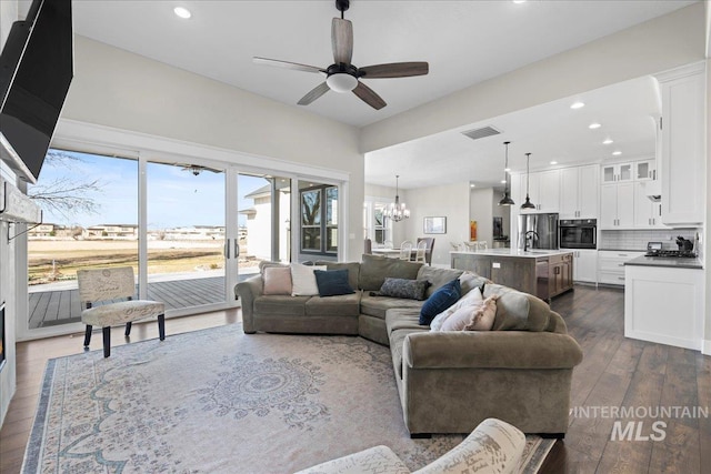 living room with recessed lighting, dark wood-style flooring, visible vents, and ceiling fan with notable chandelier