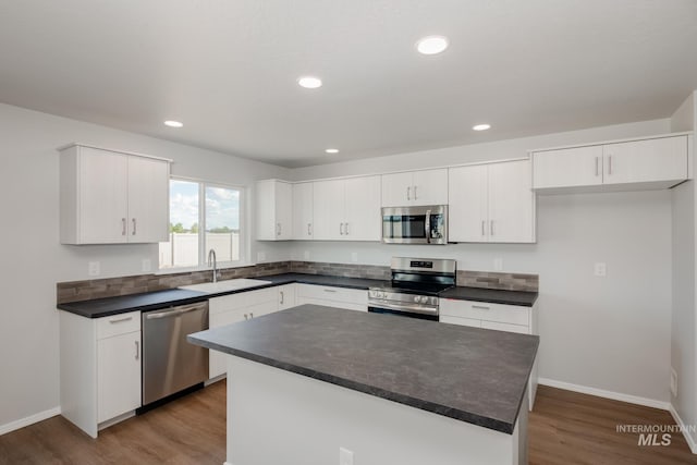 kitchen with sink, wood-type flooring, a kitchen island, stainless steel appliances, and white cabinets