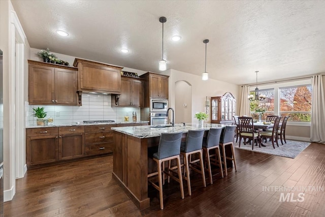 kitchen featuring dark wood finished floors, backsplash, stainless steel appliances, and light stone countertops