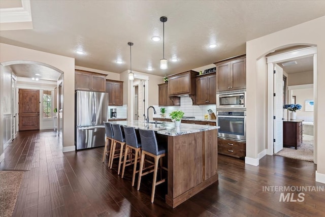 kitchen with dark wood-style flooring, backsplash, stainless steel appliances, and light stone countertops