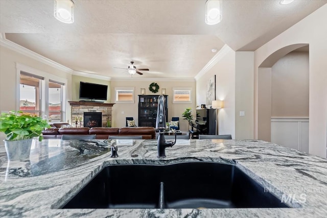 kitchen with ornamental molding, a ceiling fan, light stone counters, a sink, and a fireplace