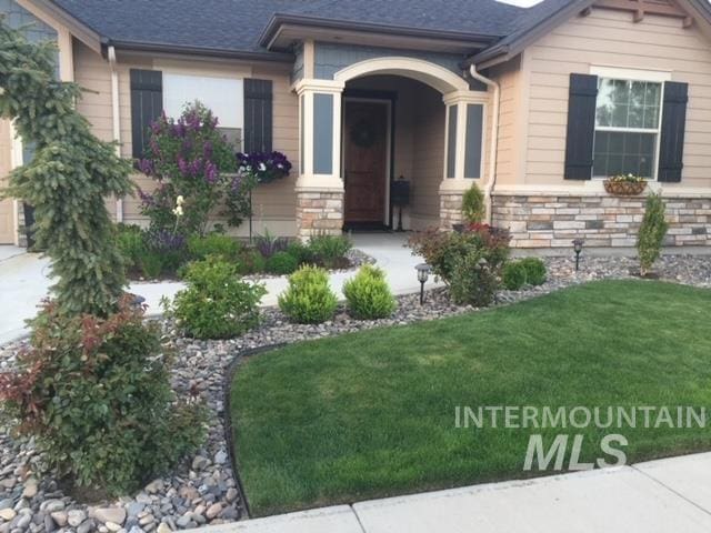 view of exterior entry featuring a lawn and stone siding