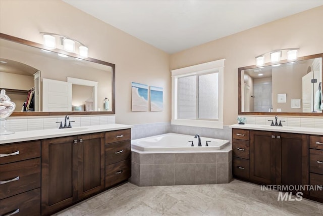 full bath with a garden tub, two vanities, backsplash, and a sink