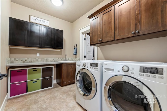 laundry area featuring washer and dryer, cabinet space, a textured ceiling, and a sink