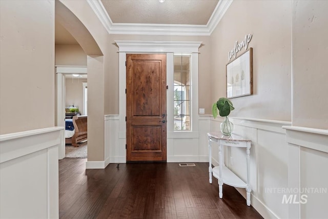 foyer entrance featuring a wainscoted wall, dark wood finished floors, arched walkways, and ornamental molding