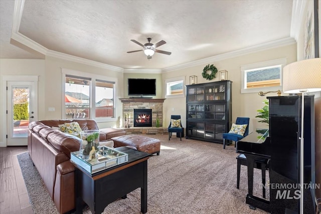 living room with a stone fireplace, crown molding, plenty of natural light, and a ceiling fan