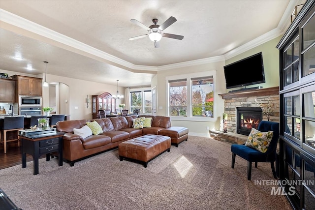 living room with baseboards, arched walkways, ceiling fan, a stone fireplace, and crown molding