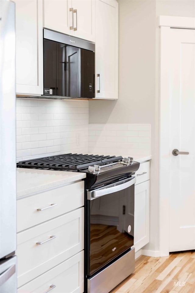 kitchen featuring light wood-style flooring, white cabinets, appliances with stainless steel finishes, decorative backsplash, and light stone countertops