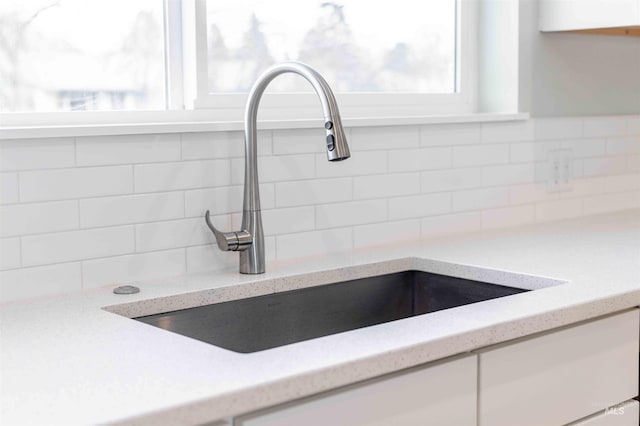 details featuring tasteful backsplash, a sink, white cabinetry, and light stone countertops