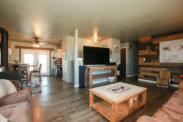 living room featuring dark hardwood / wood-style floors, ceiling fan, a wood stove, wood walls, and french doors