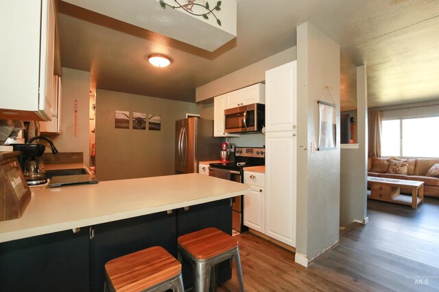 kitchen with dark hardwood / wood-style flooring, a kitchen bar, appliances with stainless steel finishes, and white cabinetry