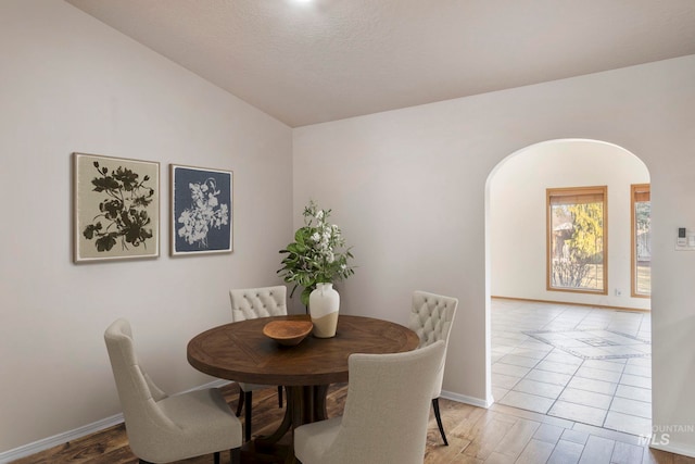 dining area featuring arched walkways, vaulted ceiling, wood finished floors, and baseboards