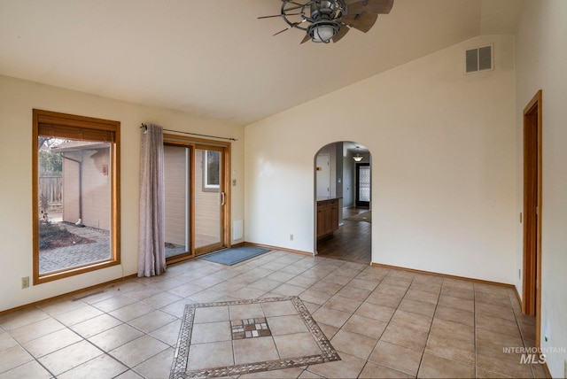 empty room featuring arched walkways, a wealth of natural light, vaulted ceiling, and visible vents