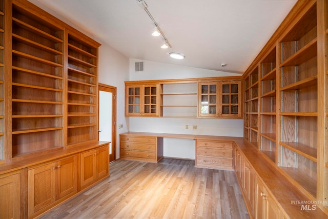 unfurnished office with visible vents, light wood-style floors, vaulted ceiling, built in desk, and rail lighting