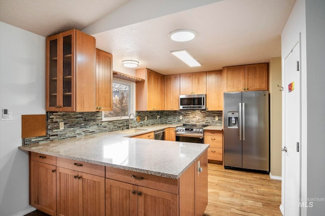 kitchen featuring light stone counters, stainless steel appliances, a sink, light wood finished floors, and glass insert cabinets