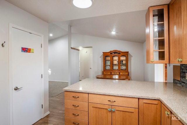 kitchen with lofted ceiling, light stone countertops, and glass insert cabinets