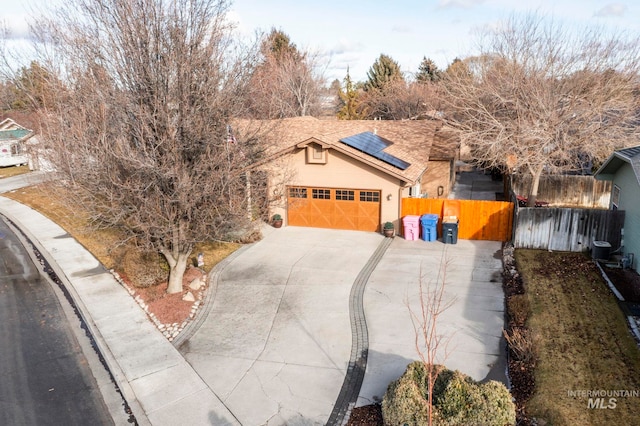 ranch-style home with driveway, an attached garage, fence, and roof mounted solar panels