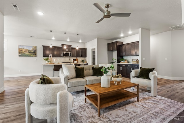 living room with baseboards, a ceiling fan, light wood finished floors, recessed lighting, and a textured ceiling