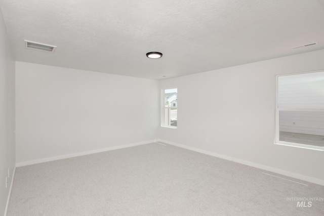 spare room featuring baseboards, a textured ceiling, visible vents, and light colored carpet