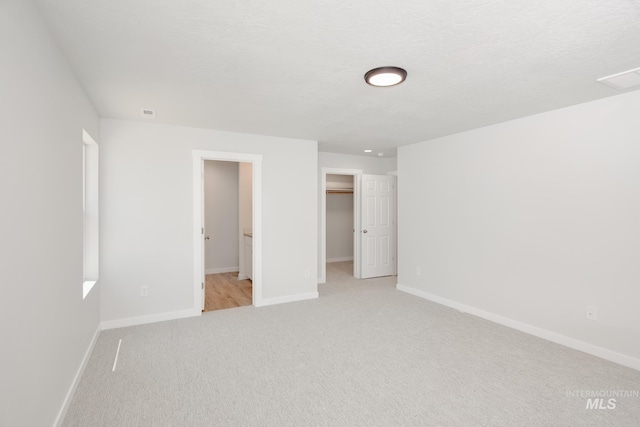 unfurnished bedroom featuring light carpet, a spacious closet, baseboards, and a textured ceiling