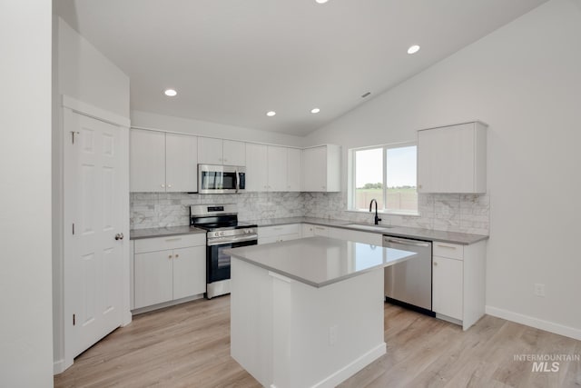 kitchen with stainless steel appliances, a kitchen island, white cabinetry, vaulted ceiling, and light countertops