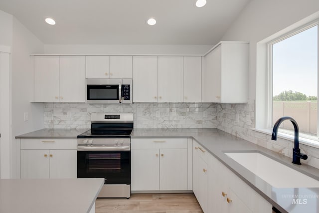 kitchen with decorative backsplash, white cabinets, appliances with stainless steel finishes, light countertops, and a sink