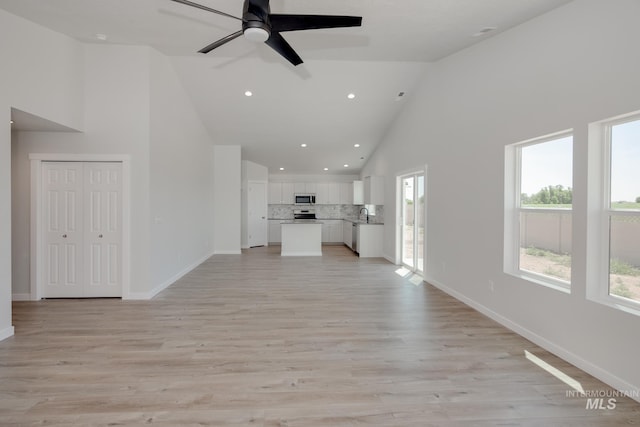 unfurnished living room featuring high vaulted ceiling, light wood-type flooring, and baseboards