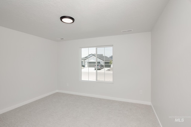 unfurnished room with carpet floors, visible vents, baseboards, and a textured ceiling