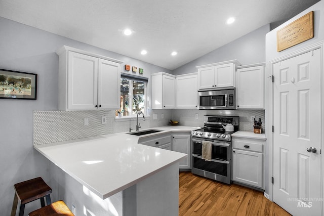 kitchen featuring kitchen peninsula, stainless steel appliances, sink, white cabinetry, and lofted ceiling