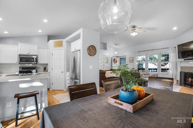 dining room with ceiling fan, light wood-type flooring, and vaulted ceiling