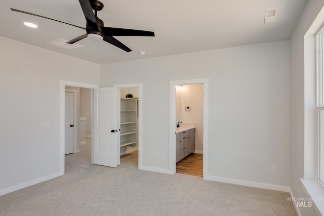 unfurnished bedroom featuring light carpet, baseboards, connected bathroom, a walk in closet, and a closet