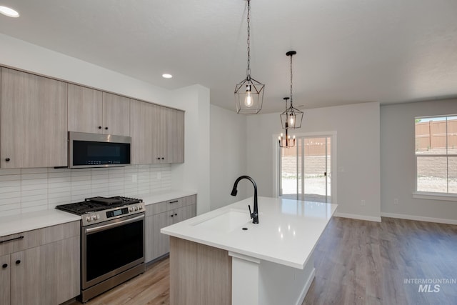 kitchen with a sink, light countertops, appliances with stainless steel finishes, tasteful backsplash, and an island with sink