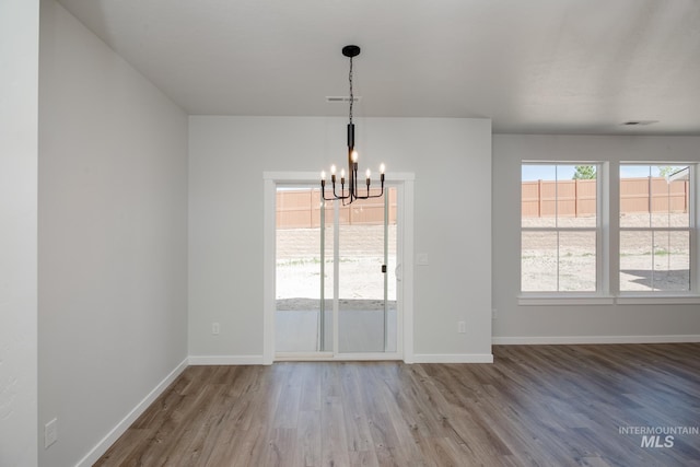 unfurnished dining area with visible vents, a notable chandelier, baseboards, and wood finished floors